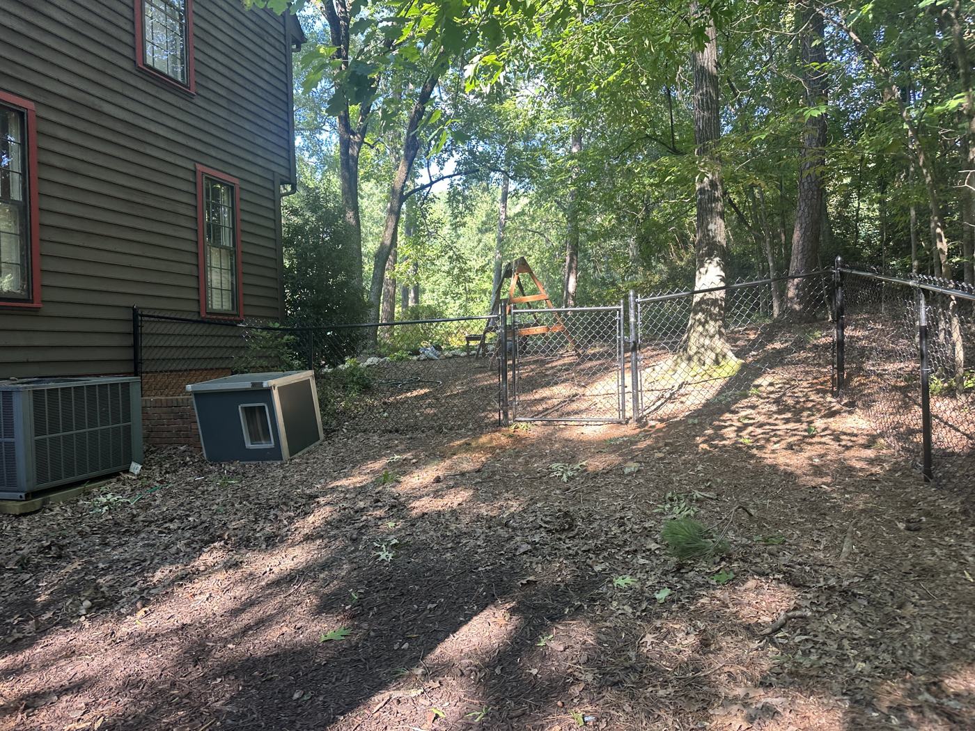 Black chain-link run through the tree line, posts set plumb on uneven ground — Precision Palmetto, Columbia SC